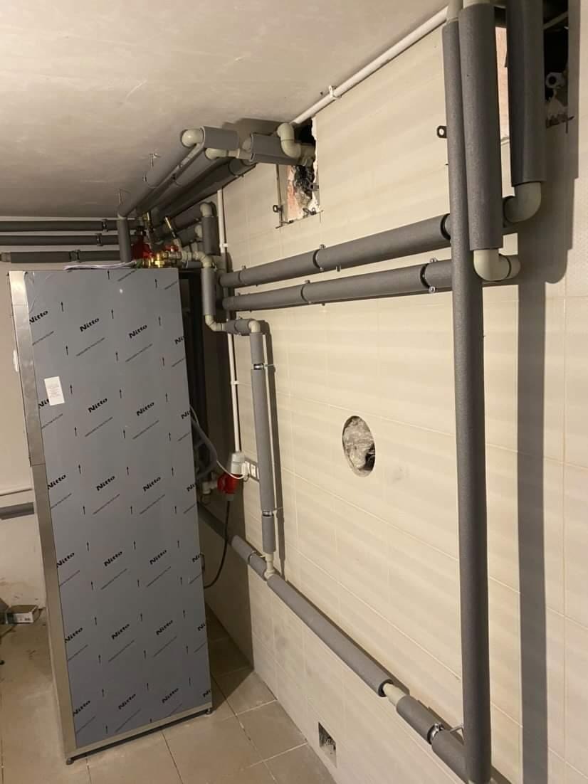 Instalacja grzewcza z rurami w izolacji termicznej, widoczny piec z obudową Nitto i fragment ściany z otworami po instalacji.