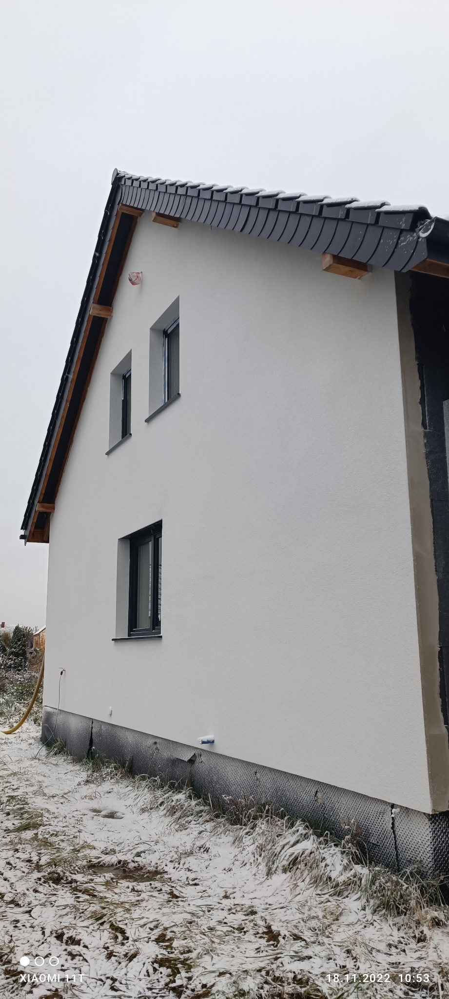 Nowo otynkowana ściana budynku w Złotoryi z widocznymi oknami o czarnych ramach i fragmentem elewacji w trakcie prac wykończeniowych, otoczona zaśnieżoną trawą.