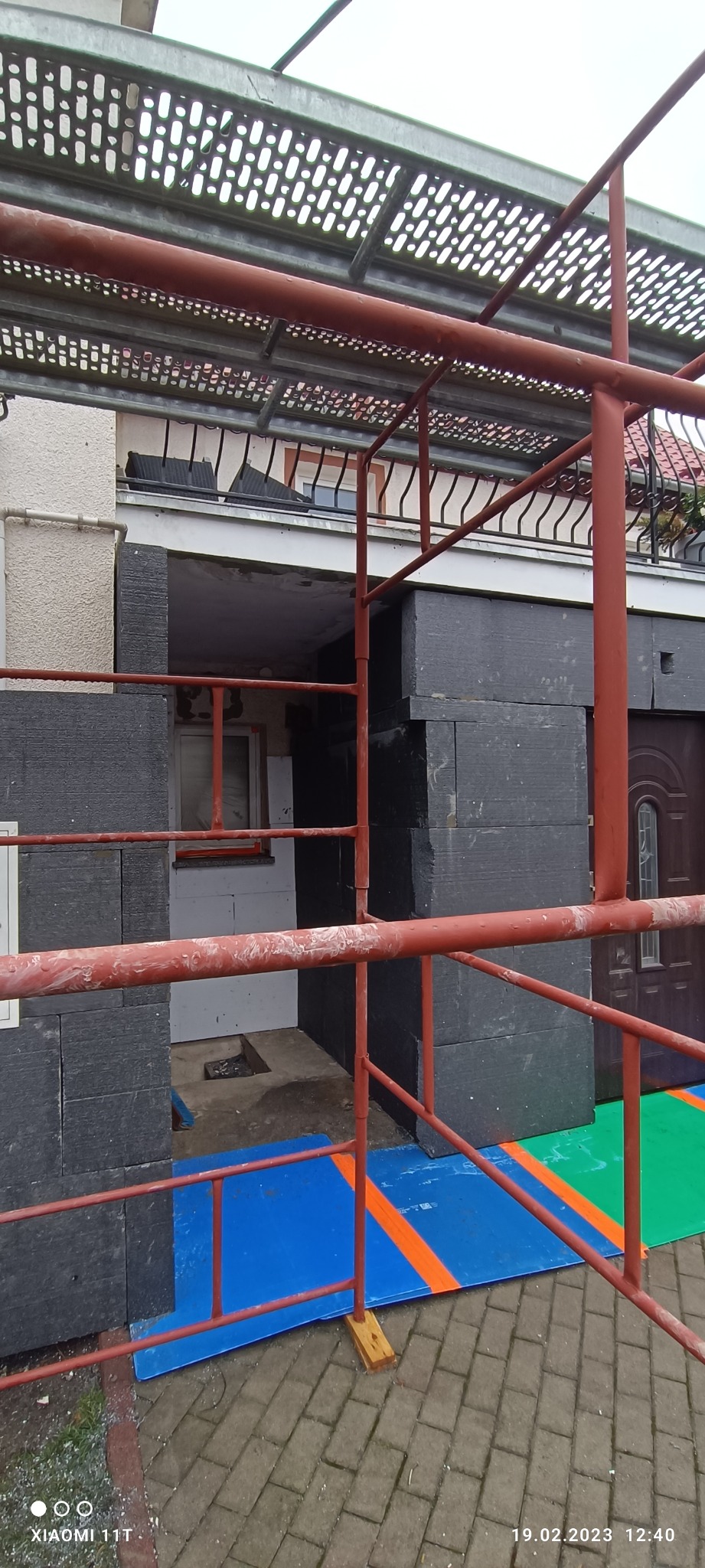 Dom w trakcie prac, widoczne rusztowanie, ocieplenie ścian styropianem grafitowym, zabezpieczenie podłoża kolorowymi płytami z tworzywa.