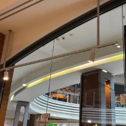 Nowoczesny system szynowy z reflektorami, zamontowany na suficie wewnątrz budynku. Widoczna instalacja oświetleniowa i fragment wnętrza z elementami cegły i szkła.