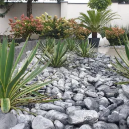 Nowoczesny ogród z szarymi kamieniami, jukami karolińskimi i hortensjami bukietowymi w odcieniach różu i kremu, z elementami małej architektury ogrodowej w tle.