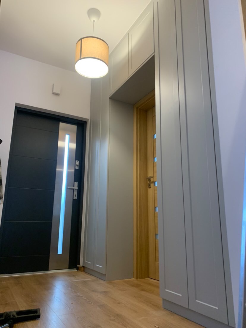 Szare szafy w zabudowie w przedpokoju, z widoczną lampą sufitową i dwiema parami drzwi w tle.