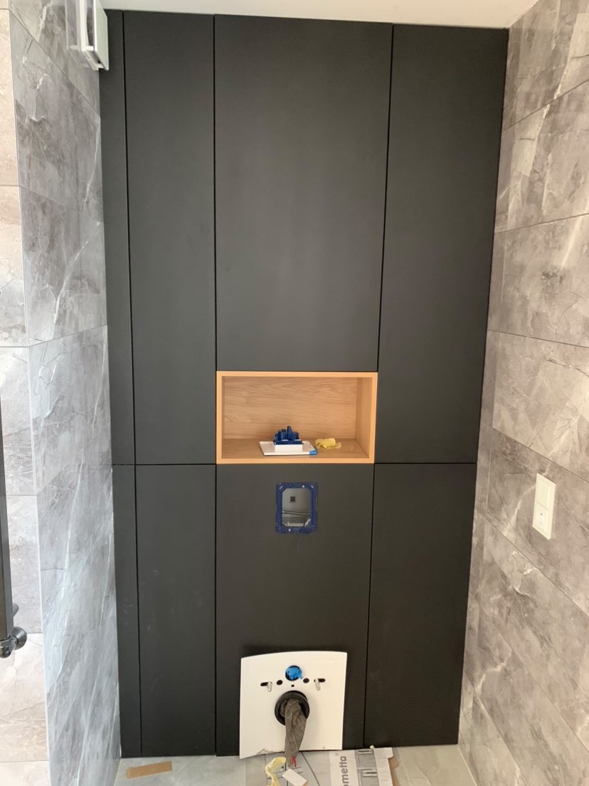 Montaż podtynkowego stelaża WC z szafką wnękową w łazience wykończonej szarym marmurem, widoczne elementy instalacyjne przed zabudową.