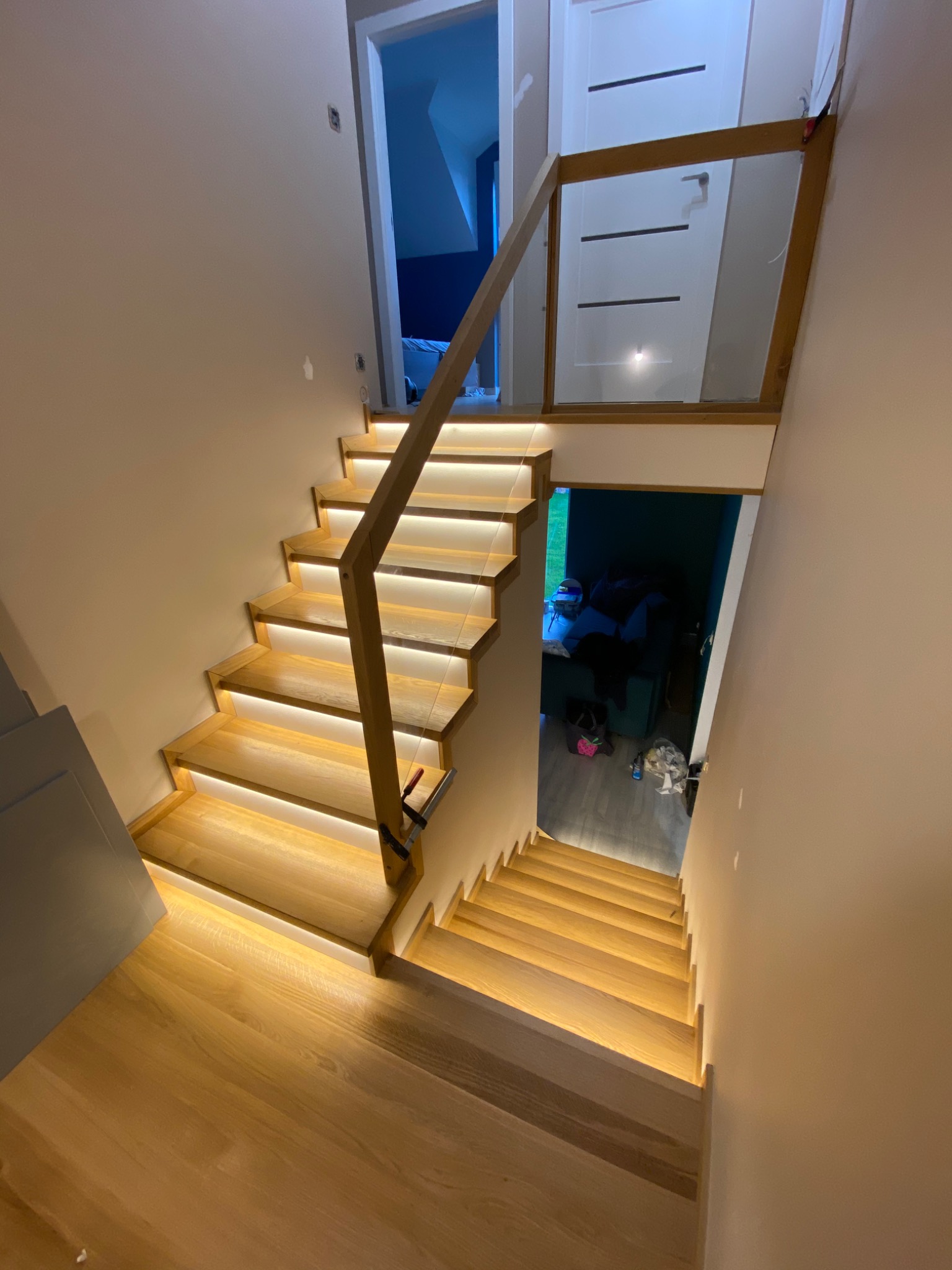 Drewniane schody z podświetleniem LED, szklana balustrada, widok z góry na dół, drzwi w tle.