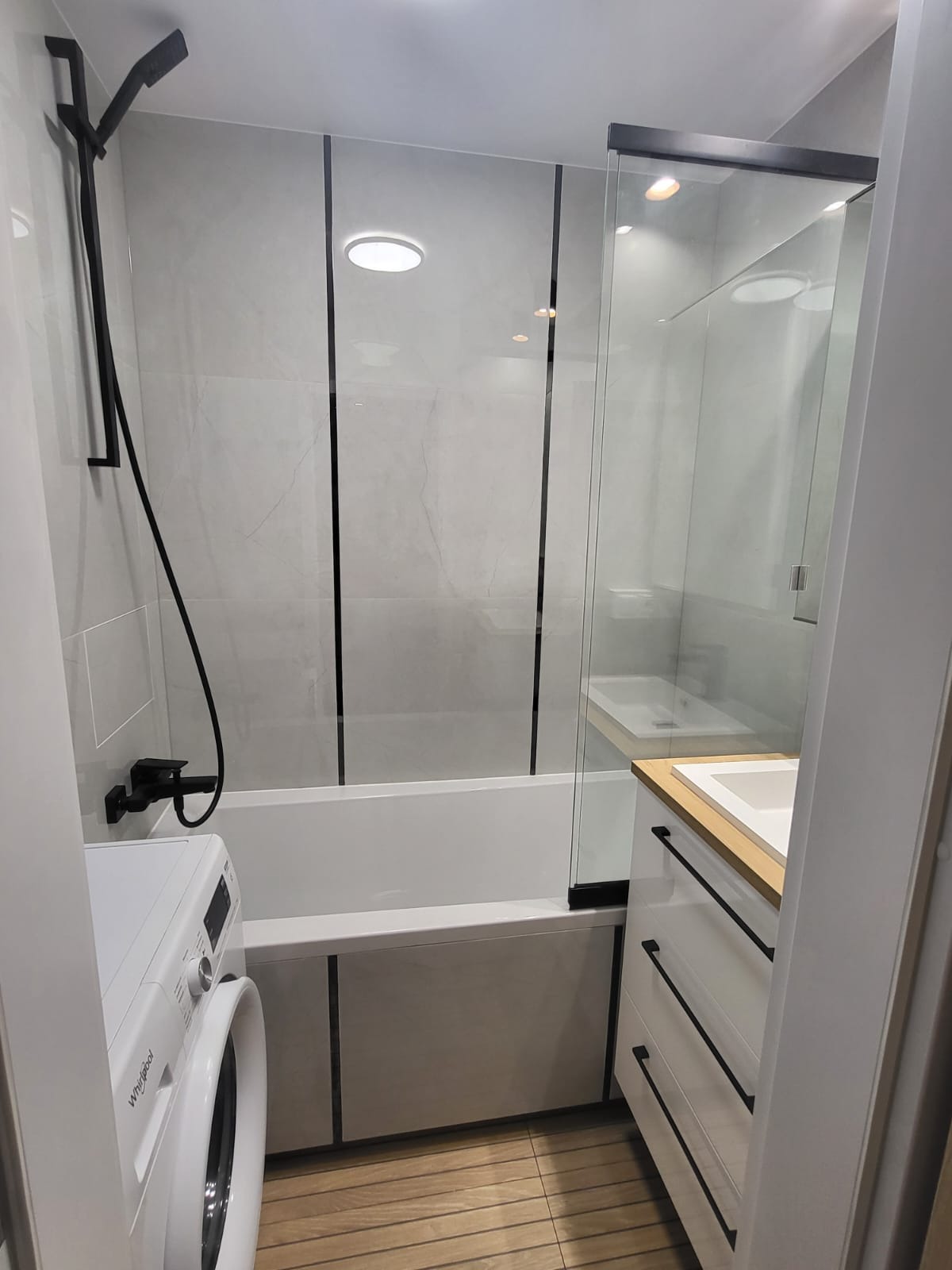 Nowoczesna aranżacja łazienki we Wrocławiu z wanną obudowaną płytkami, szklanym parawanem nawannowym, armaturą w kolorze czarnym i pralką.