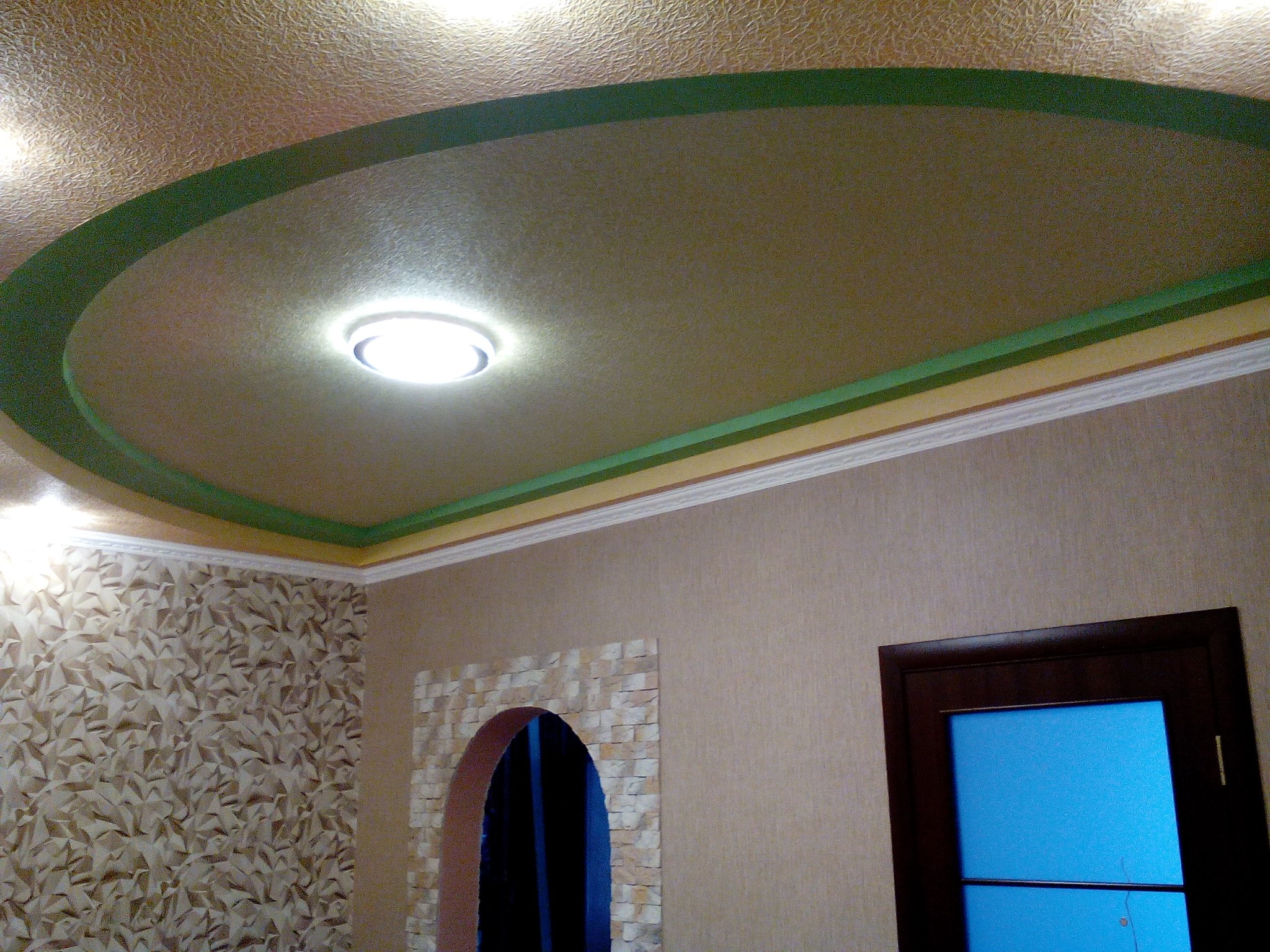 Sufit podwieszany z oświetleniem punktowym, dekoracyjną sztukaterią i malowaniem w odcieniach beżu i zieleni, ściana z tapetą o wzorze geometrycznym i dekoracyjnym łukiem.