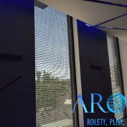 Wnętrze pokoju z oknem osłoniętym poziomymi lamelami, widok na zieleń za oknem, dekoracyjne oświetlenie sufitowe w odcieniach niebieskiego.