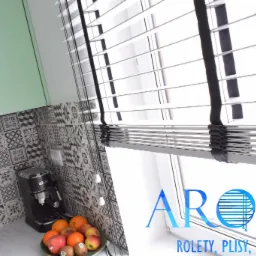 Białe poziome listwy z czarną taśmą na oknie w kuchni z wzorzystymi płytkami, ekspresem do kawy i miską owoców, widoczne logo firmy.