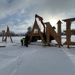 SG-USŁUGI - Montaż dużych, drewnianych liter dekoracyjnych na śniegu przy użyciu dźwigu samochodowego, widoczni robotnicy w odblaskowych kamizelkach.
