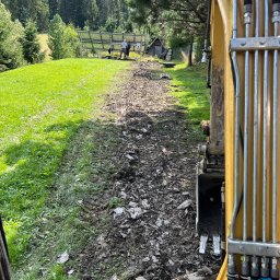 SG-USŁUGI - Żółta koparka na skraju wykopu, w tle panele słoneczne i zielone wzgórze.