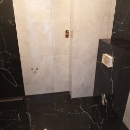 Maciej Flaga Żurawie - Nowoczesna łazienka z czarno-białymi marmurkowymi płytkami, widoczne podłączenia armatury na ścianie i zabudowa geberit, minimalistyczny design.