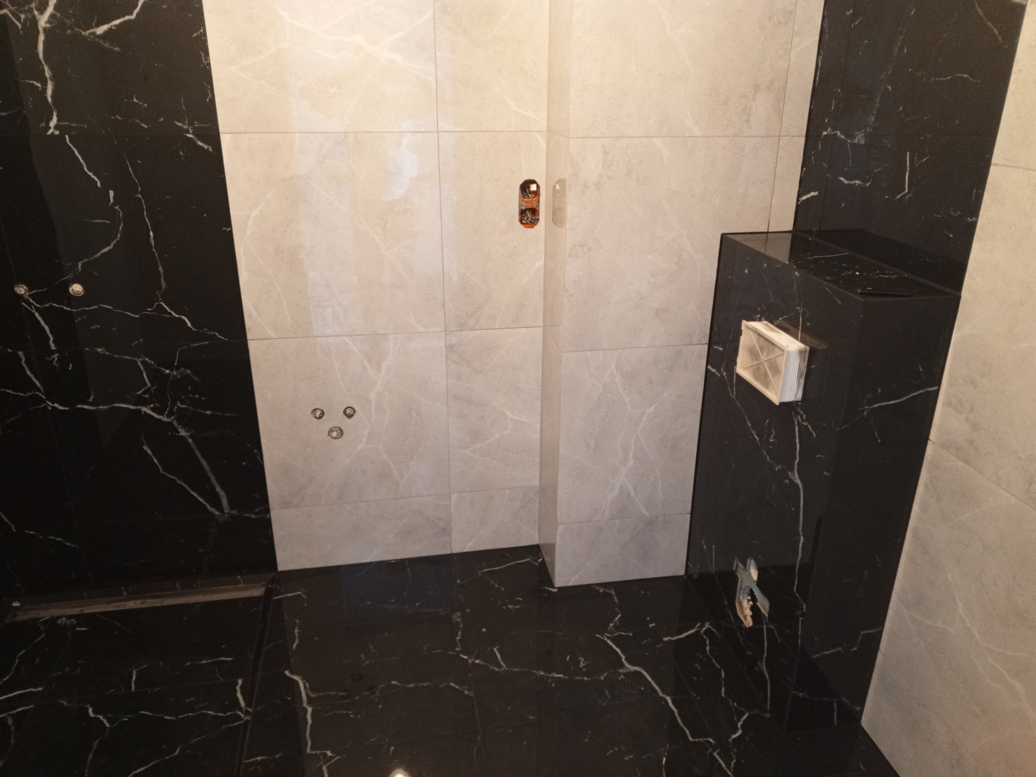 Nowoczesna łazienka z czarno-białymi marmurkowymi płytkami, widoczne podłączenia armatury na ścianie i zabudowa geberit, minimalistyczny design.