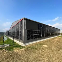 Duży budynek przemysłowy pokryty panelami słonecznymi, widok z zewnątrz w słoneczny dzień.