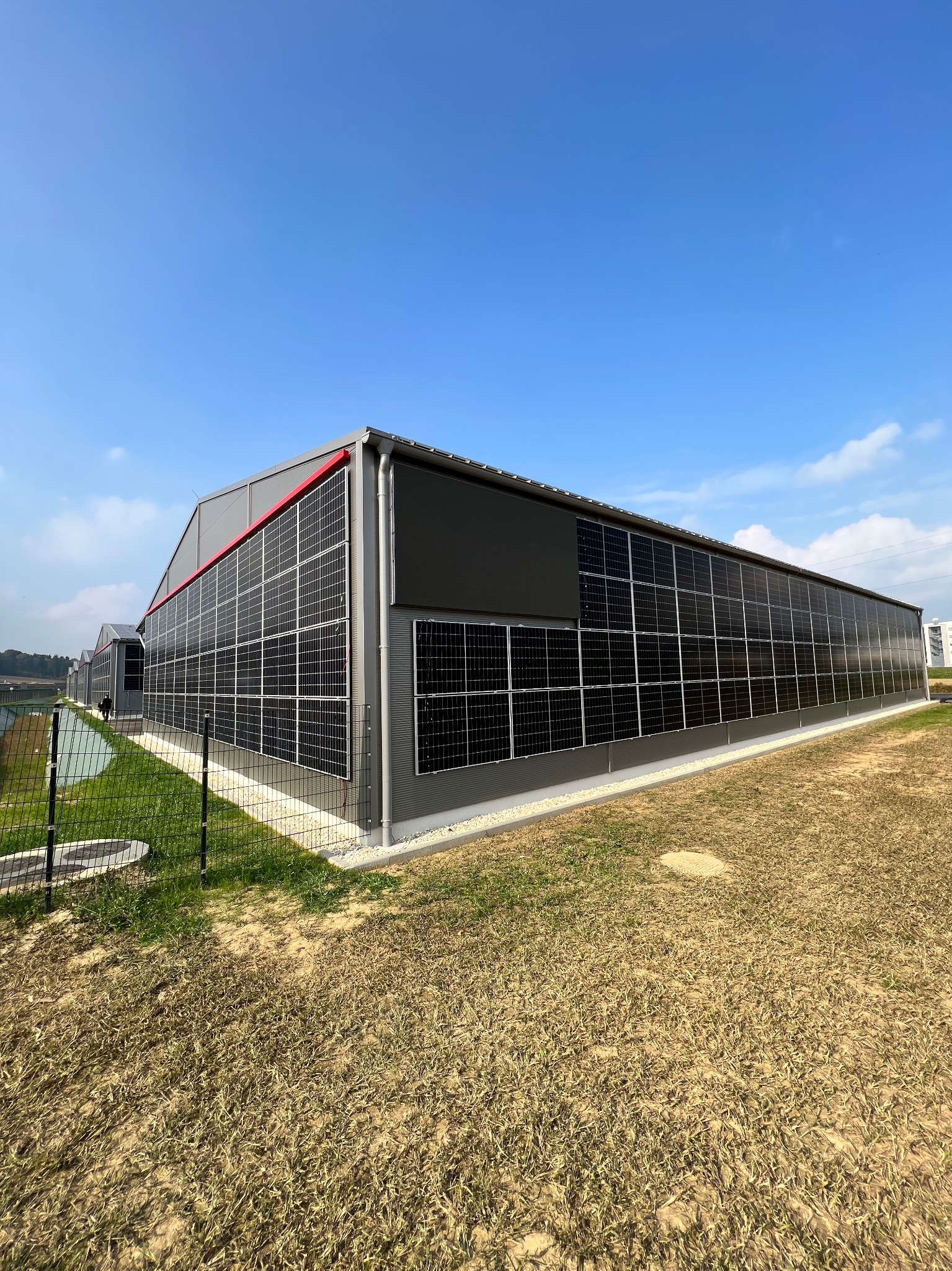 Duży budynek przemysłowy pokryty panelami słonecznymi, widok z zewnątrz w słoneczny dzień.