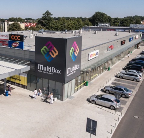 Widok z góry na park handlowy MultiBox z parkingiem i logotypem na elewacji, prezentujący architekturę budynku i otoczenie.