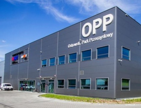 Szara hala przemysłowa z napisem 'OPP Ostrowski Park Przemysłowy', biały van i rower zaparkowane przed wejściem.