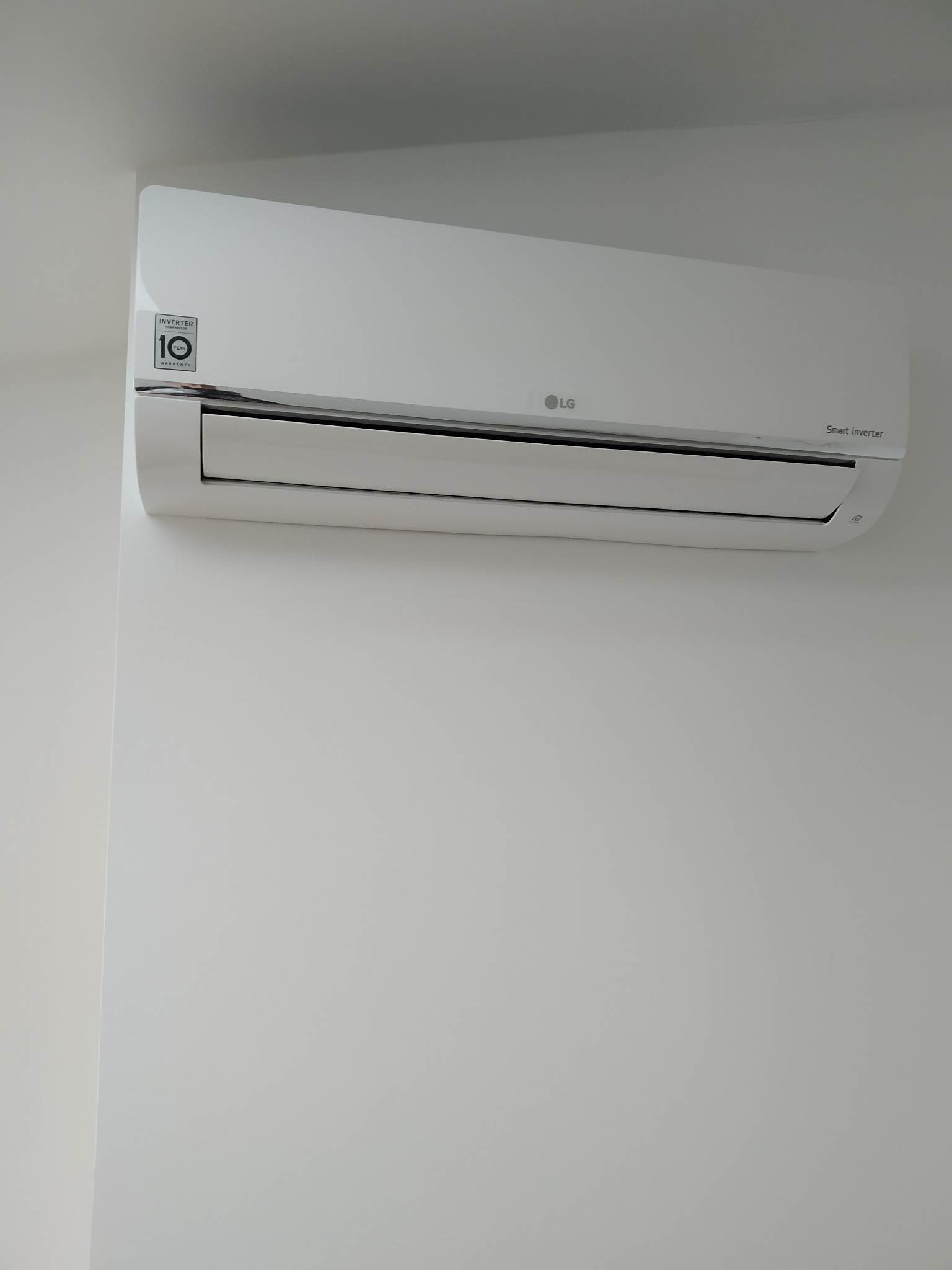 Biały klimatyzator LG Smart Inverter zamontowany na jasnej ścianie, widoczna naklejka z 10-letnią gwarancją na kompresor.