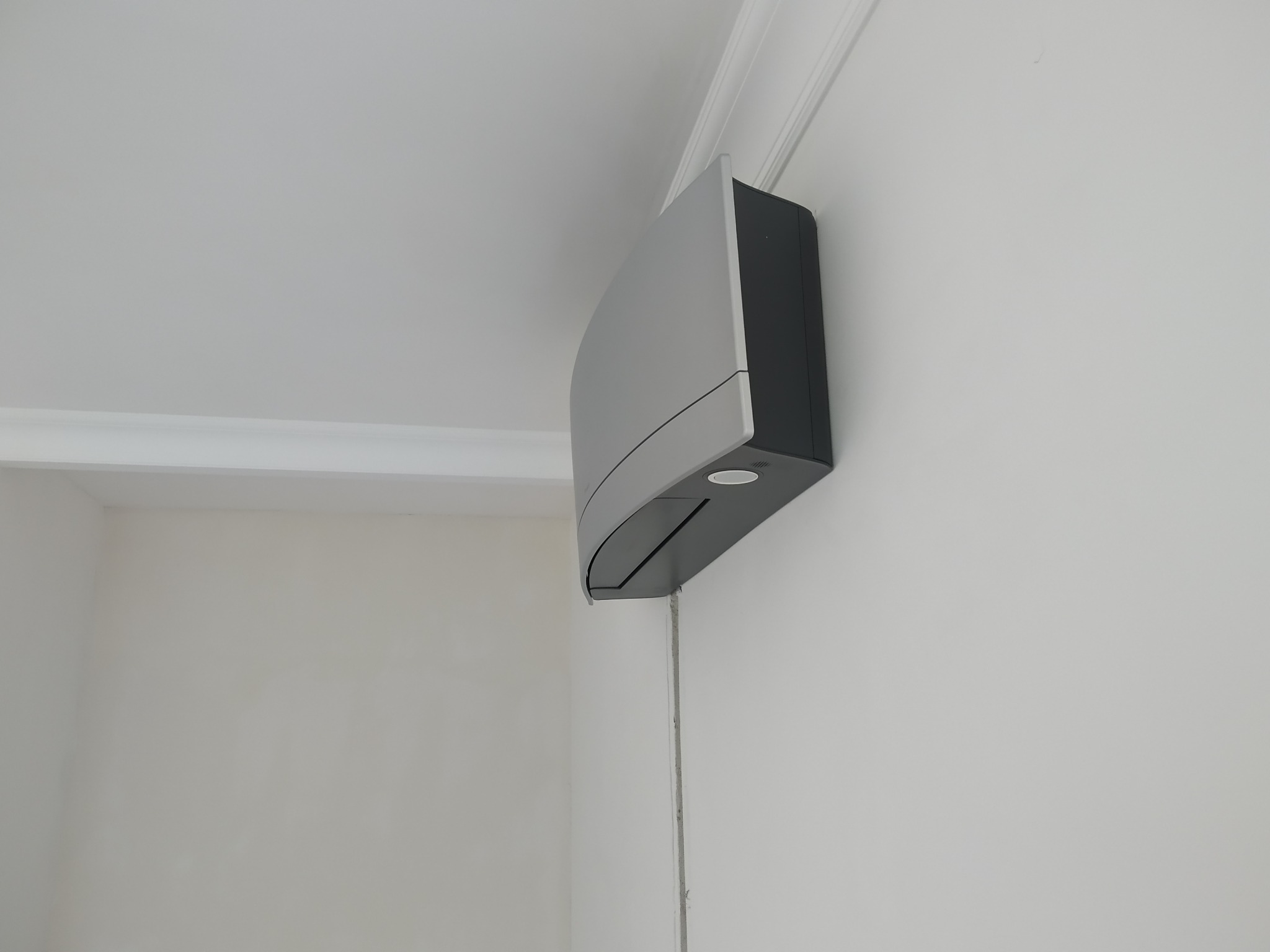 Zamontowana na ścianie, nowoczesna klimatyzacja w kolorze srebrnym, z widoczną listwą przypodłogową i gładką, białą ścianą w tle.