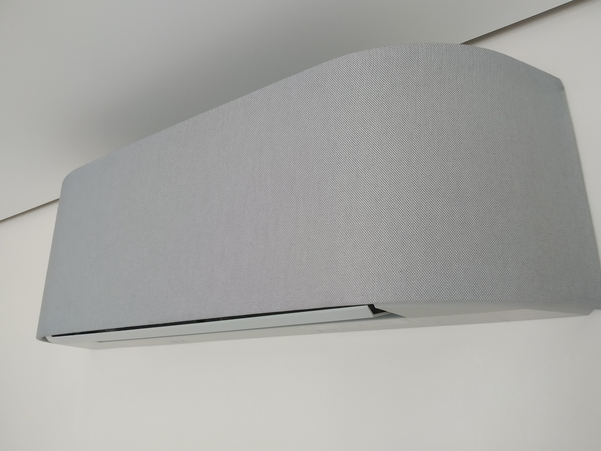 Nowoczesny klimatyzator ścienny z szarą, teksturowaną obudową, zamontowany na białej ścianie, widoczny z perspektywy lekko od dołu.