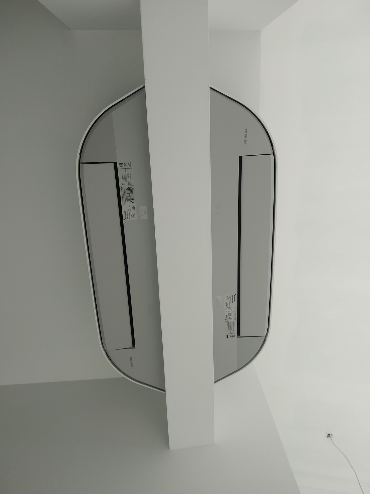 Biały klimatyzator Toshiba zamontowany na suficie, częściowo zasłonięty przez pionową belkę konstrukcyjną.