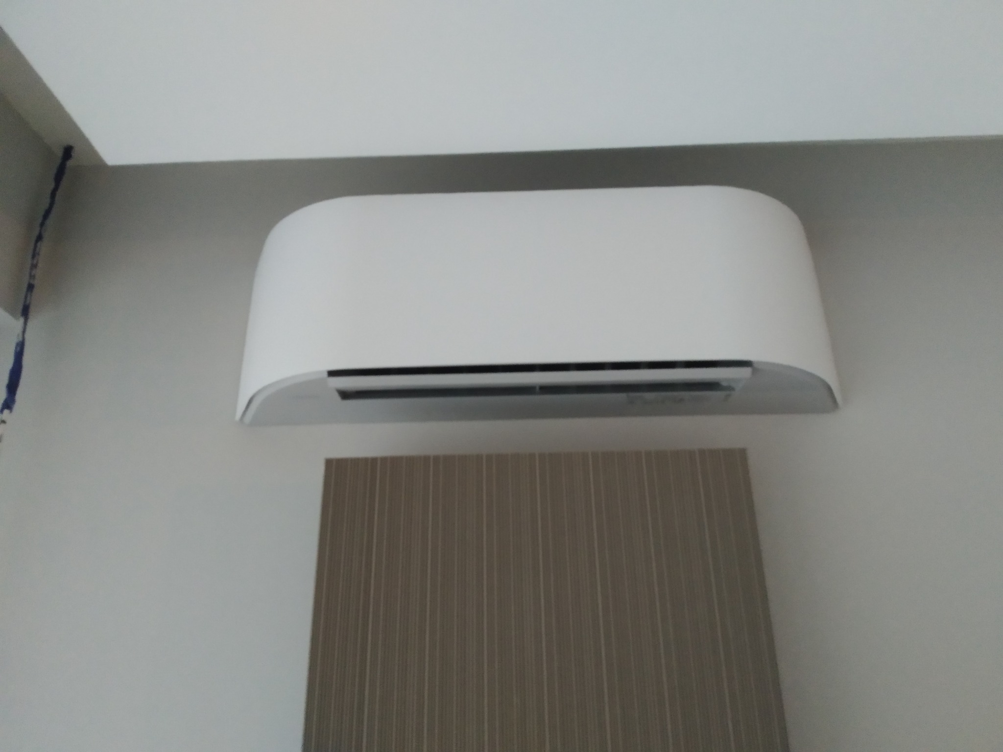 Biały klimatyzator ścienny zamontowany w pomieszczeniu z dekoracyjną ścianą w pionowe paski.