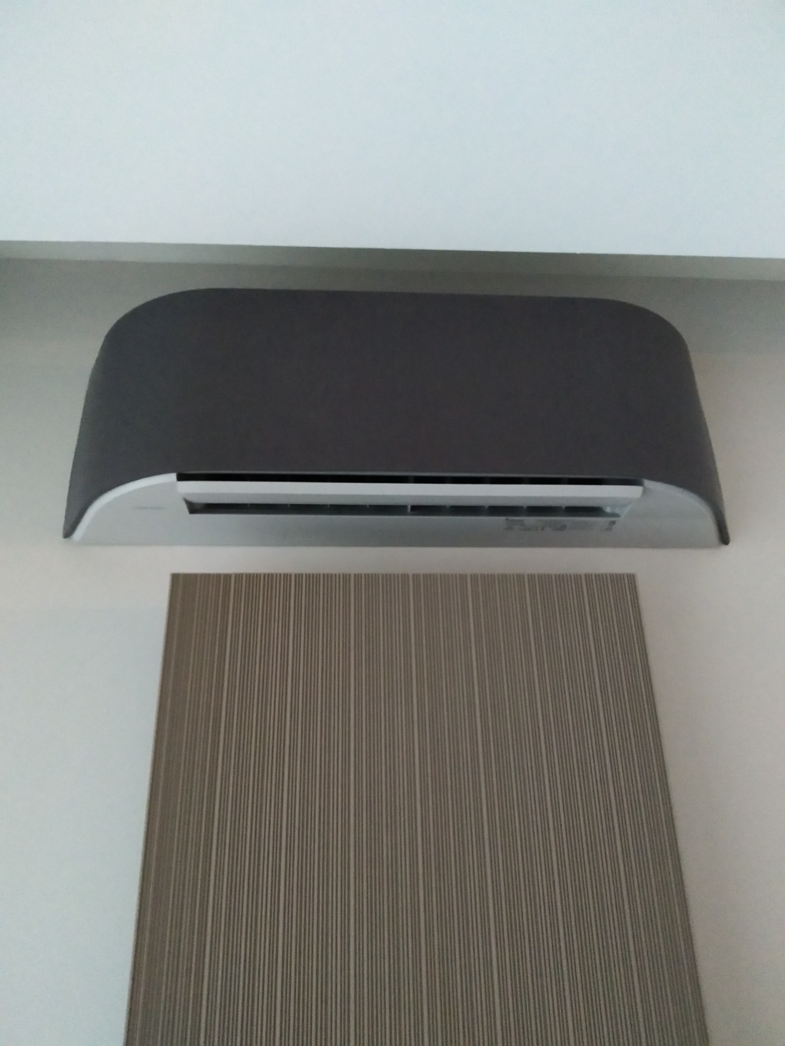 Nowoczesny, szary klimatyzator ścienny z panelem dekoracyjnym w tle, zamontowany na białej ścianie.