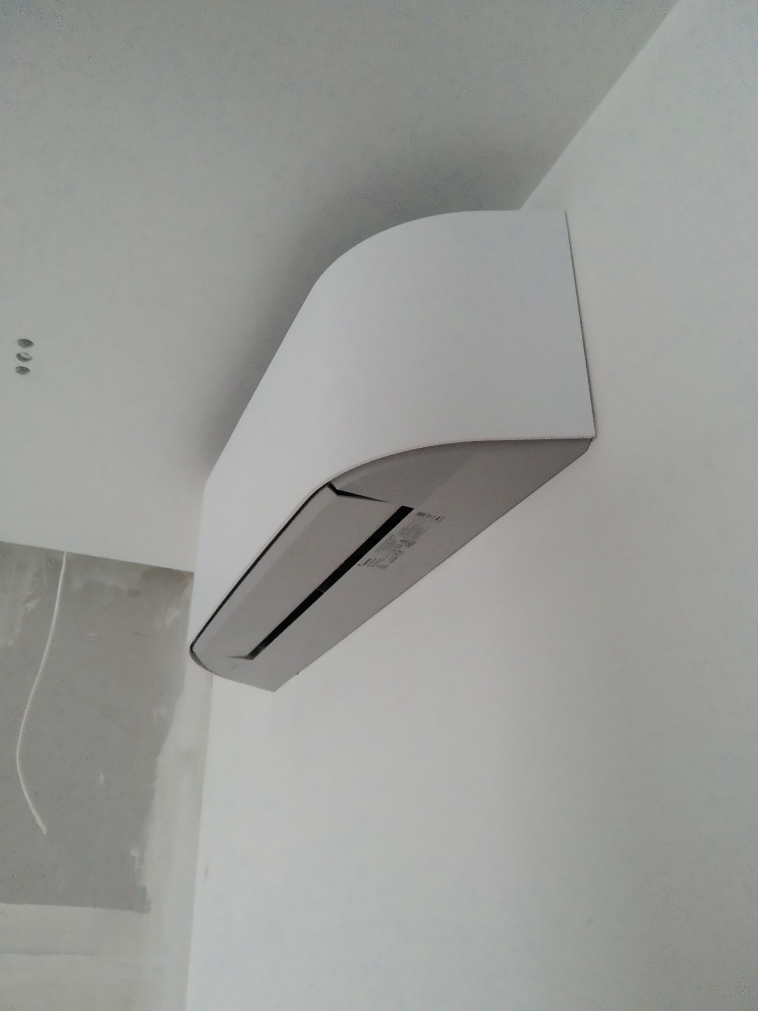 Biała jednostka klimatyzacji, zamontowana na ścianie w trakcie remontu, widoczne ślady gładzi i niedokończone wykończenie.