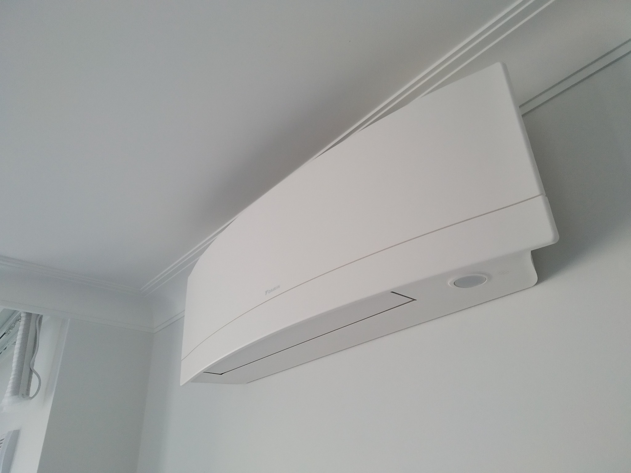 Biały klimatyzator Daikin zamontowany na ścianie w jasnym pomieszczeniu, widoczne listwy przysufitowe.