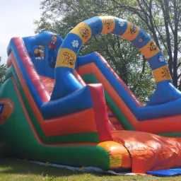 Kolorowa, nadmuchiwana zjeżdżalnia dla dzieci z motywem bajki Psi Patrol, ustawiona na trawie w ogrodzie.