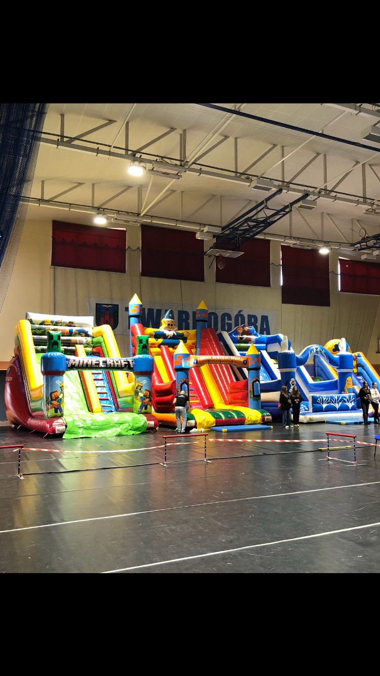 Rozstawione kolorowe dmuchane zamki i zjeżdżalnie w hali sportowej, z motywami z gier i postaci z bajek.