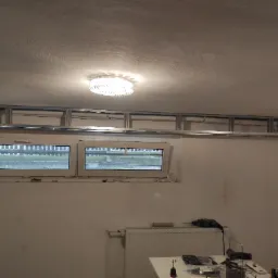 Metalowa konstrukcja pod sufitem, prawdopodobnie pod montaż płyty karton gips, widoczne okna, grzejnik i narzędzia na stole.