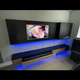 Czarna zabudowa meblowa na ścianie z podświetleniem LED, nowoczesny salon z telewizorem i szafkami wiszącymi.