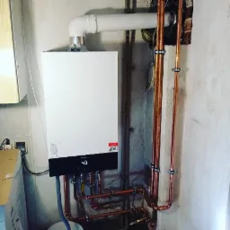 Nowoczesny, biały piec gazowy Viessmann z cyfrowym wyświetlaczem temperatury (40 stopni Celsjusza), zamontowany na szarej, surowej ścianie. Widoczne miedziane rury instalacji grzewczej z metalowymi...