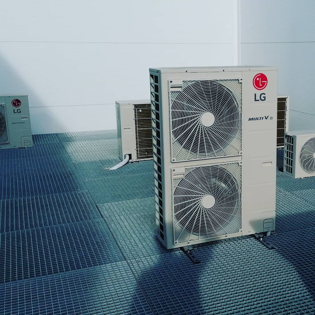 Instalacja klimatyzacji LG Multi V 8 na dachu z kratą pomostową, widoczne jednostki zewnętrzne z białymi przewodami.