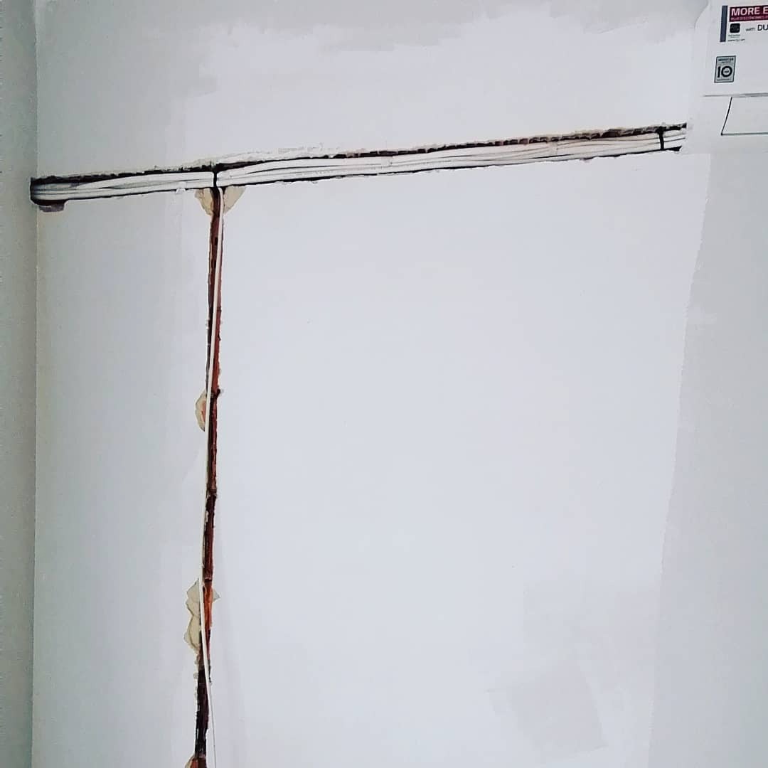 Biała ściana z wyżłobionymi bruzdami pionową i poziomą, przygotowanymi pod instalację, widoczny fragment klimatyzatora LG w prawym górnym rogu.