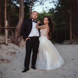 FOTSWIM MICHAŁ DEREWECKI - Para młoda na plaży w lesie: on w smokingu, ona w sukni z odkrytymi plecami i tatuażem. Romantyczna sesja ślubna w naturalnym otoczeniu.