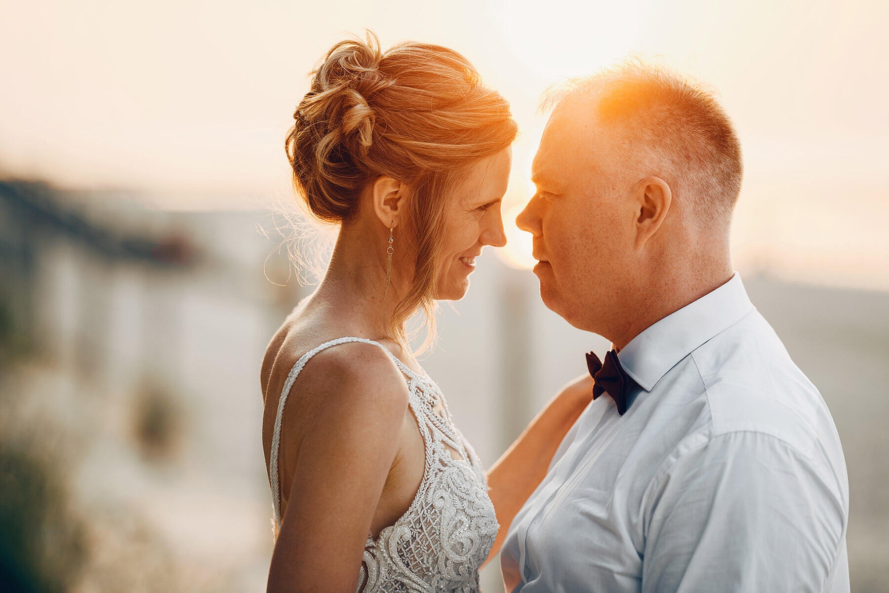Para wpatrzona w siebie podczas zachodu słońca, kobieta w koronkowej sukni, mężczyzna w białej koszuli i muszce