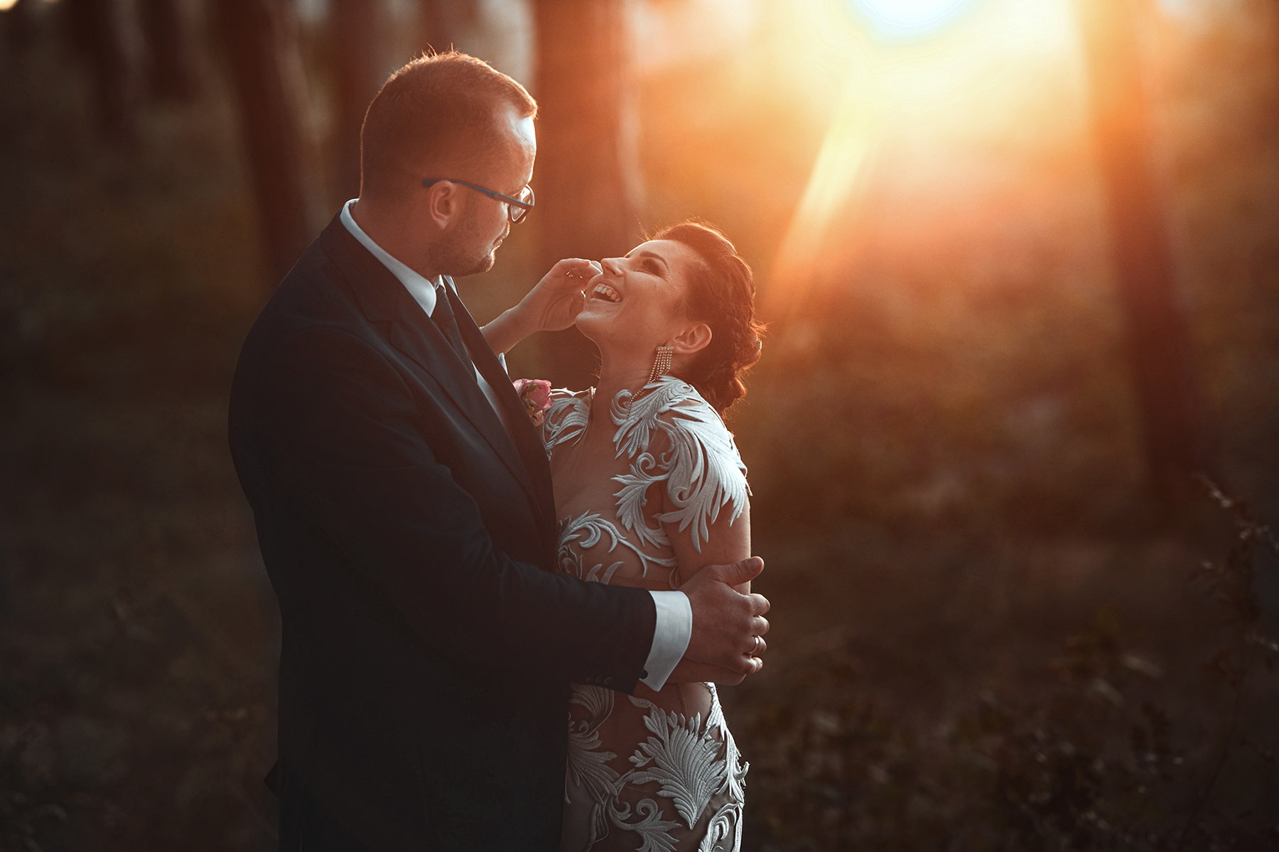 Para młoda w Koszalinie w objęciach, panna młoda w sukni z koronkowymi aplikacjami, delikatne światło słoneczne.