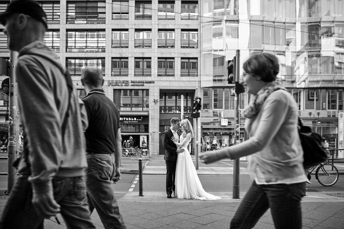 Para młoda w czarno-białej sesji ślubnej pośrodku ruchliwej ulicy miejskiej, z przechodniami w tle i na pierwszym planie.