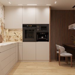 PROJEKTORNIA.COM.PL - Nowoczesna kuchnia z beżowymi frontami szafek, marmurowym blatem i ścianą, zabudowanym piekarnikiem, mikrofalówką i ekspresem do kawy, oraz drewnianą ścianą z lamelami w tle jadalni z szarymi...