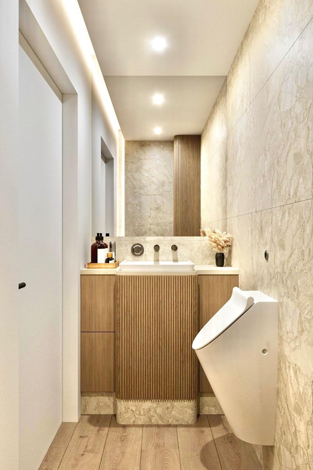Wąska łazienka z marmurowymi płytkami, wiszącą muszlą klozetową, umywalką na szafce z lamelami i podświetlanym lustrem.