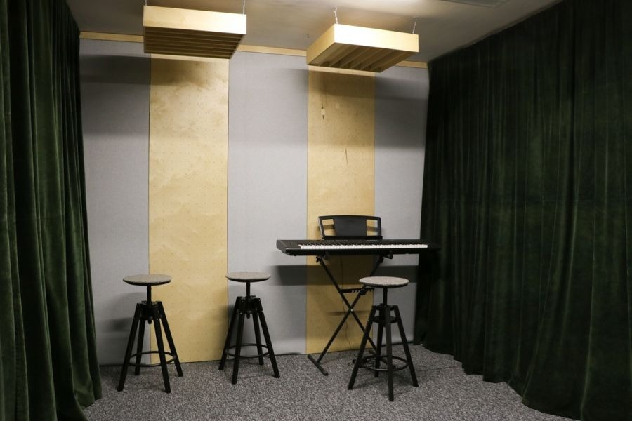 Wnętrze pokoju do nagrywania w Obornikach Śląskich z pianinem, trzema stołkami i akustycznymi panelami na ścianach, zasłonięte zielonymi kotarami.