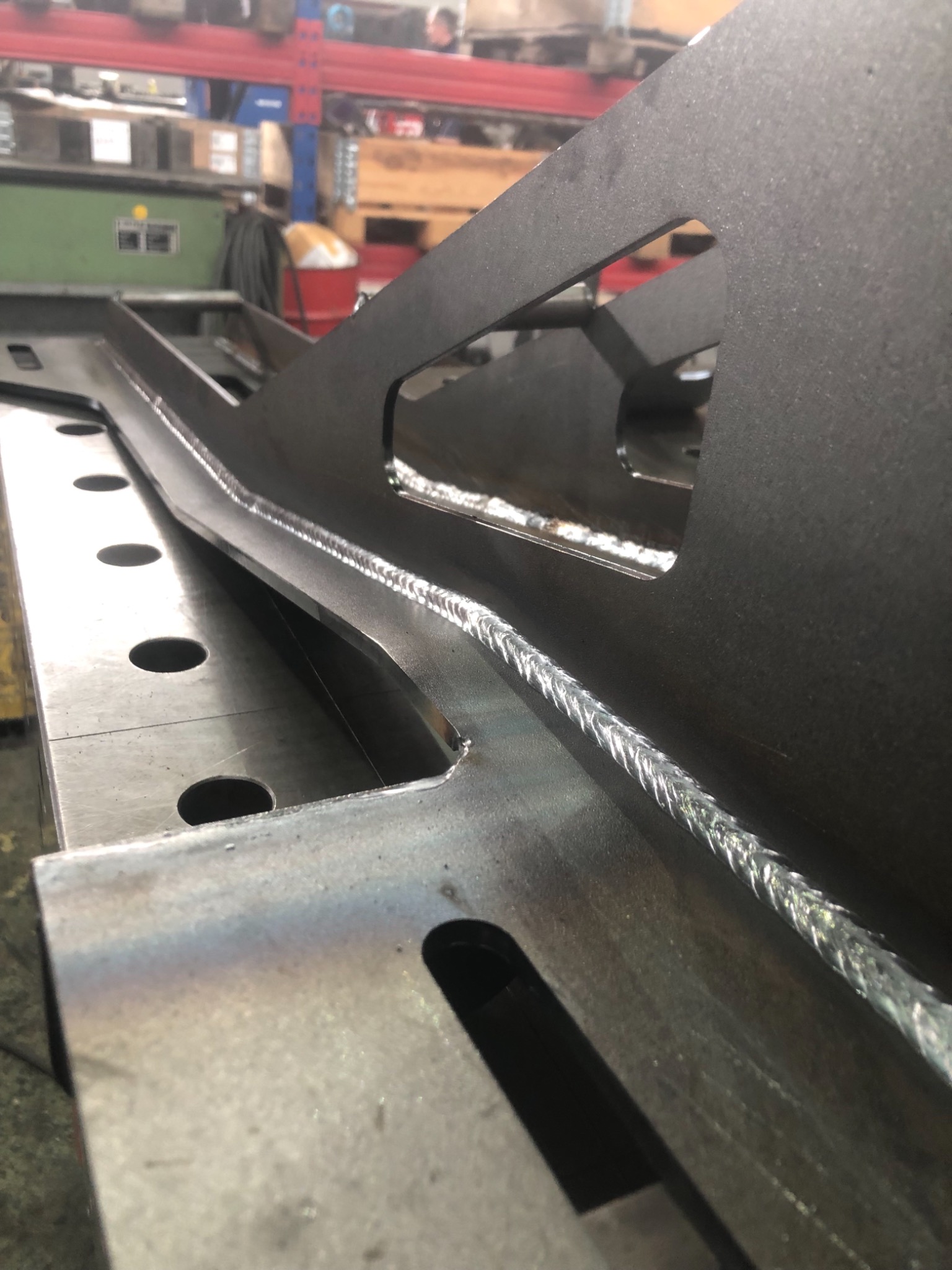 Szczegółowe zbliżenie na świeżo wykonany spaw na metalowej konstrukcji z otworami, ukazujący precyzję i jakość łączenia.