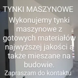 Świeżo otynkowana ściana wewnątrz budynku, z widocznym tekstem reklamowym o wykonywaniu tynków z gotowych materiałów i mieszanych na budowie.