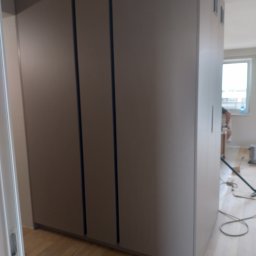 Griffin House - Wnętrze z dużą, zabudowaną szafą na wymiar w odcieniach szarości, widoczne panele podłogowe i osoba w tle, potencjalnie podczas montażu.