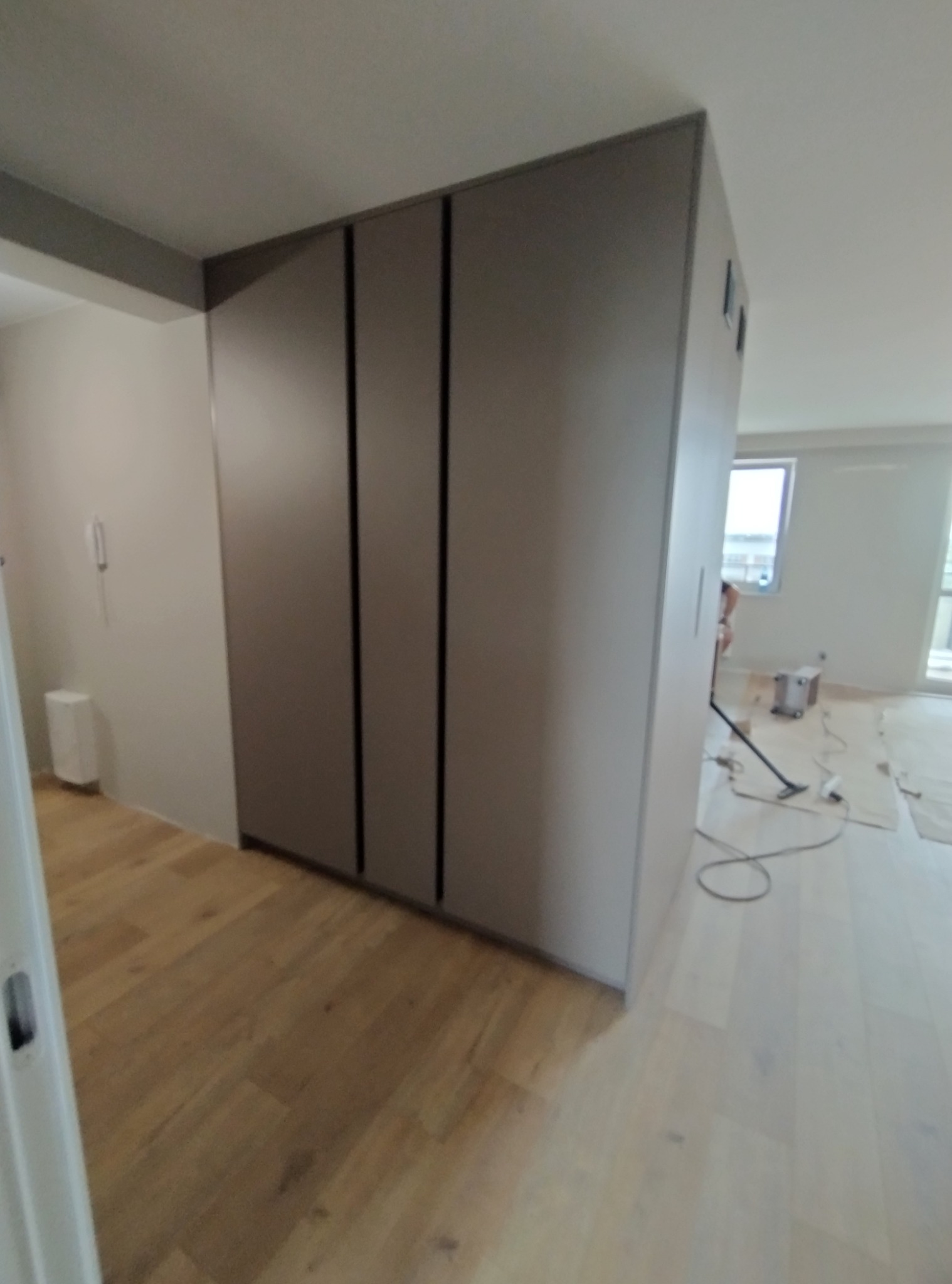 Wnętrze mieszkania w trakcie sprzątania po montażu szafy wnękowej z przesuwnymi drzwiami, widoczny odkurzacz i częściowo zakryte podłogi.