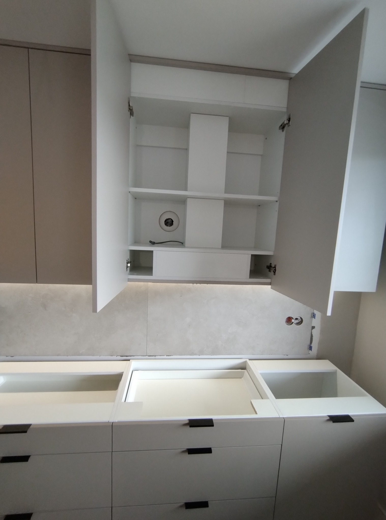 Białe, nowoczesne szafki kuchenne z otwartymi drzwiczkami górnymi, widoczne półki i oświetlenie LED pod szafkami, czarne uchwyty szuflad.