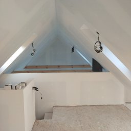 BWG- Big Work Group - Poddasze w trakcie adaptacji: białe ściany szczytowe, drewniana konstrukcja więźby dachowej, surowa podłoga z płyt OSB, zwisające przewody elektryczne i kartony z osprzętem.