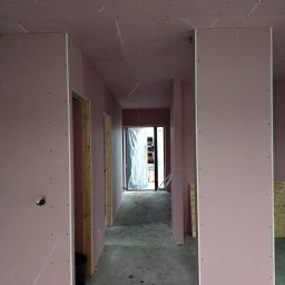 BWG- Big Work Group - Korytarz w trakcie montażu płyt gipsowo-kartonowych o różowym zabarwieniu, widoczne drewniane ościeżnice drzwiowe i surowy beton na podłodze.