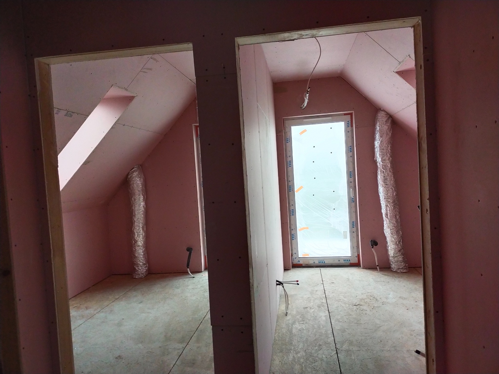 Poddasze w trakcie adaptacji: widoczne ocieplone skosy, ściany działowe z płyt gipsowo-kartonowych, okno z folią ochronną i aluminiowy przewód wentylacyjny.